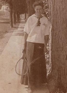 Eleanor Douglass standing outdoors holding a tennis racquet, sepia photograph